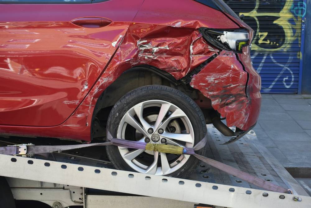 A red car with a crushed rear side on a tow truck