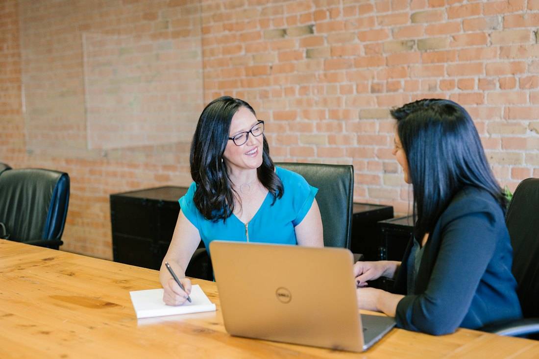 Two women talking at a table with a laptop
